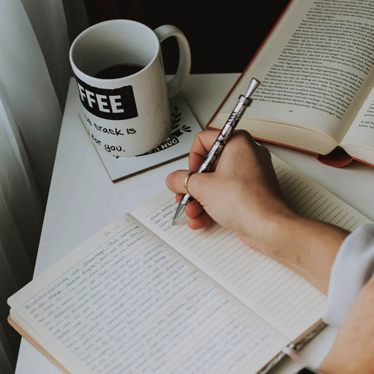 Writing in in notebook with a cup of coffee and a book on table