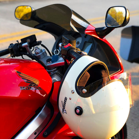 White helmet with Shoppe 815 sticker hanging off the handle bars of red Honda motorcycle