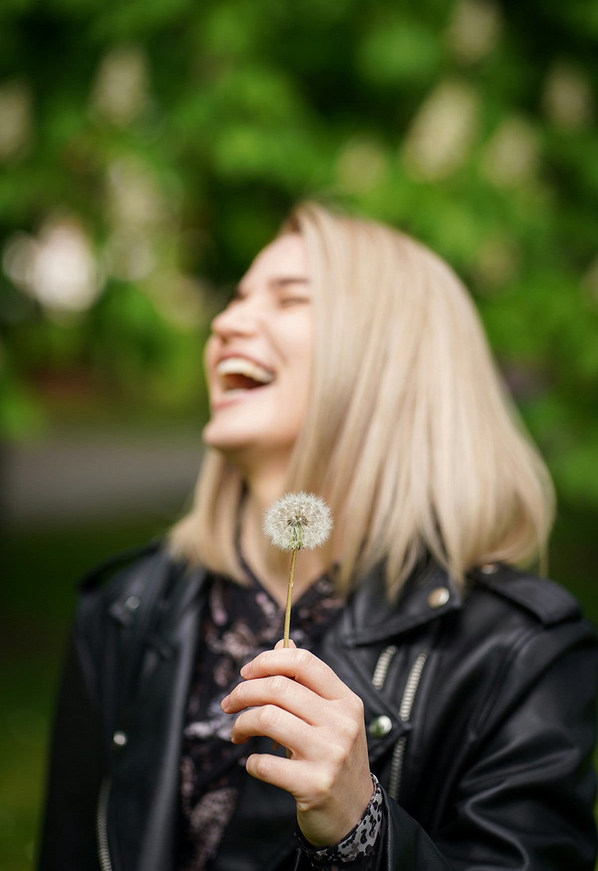 A girl in a leather motorcycle jacket laughing while holding a dandelion enjoying a chilly spring day, enjoying the smell of oakmoss covered trees.  A simple moment that will ignite memories for years to come! 