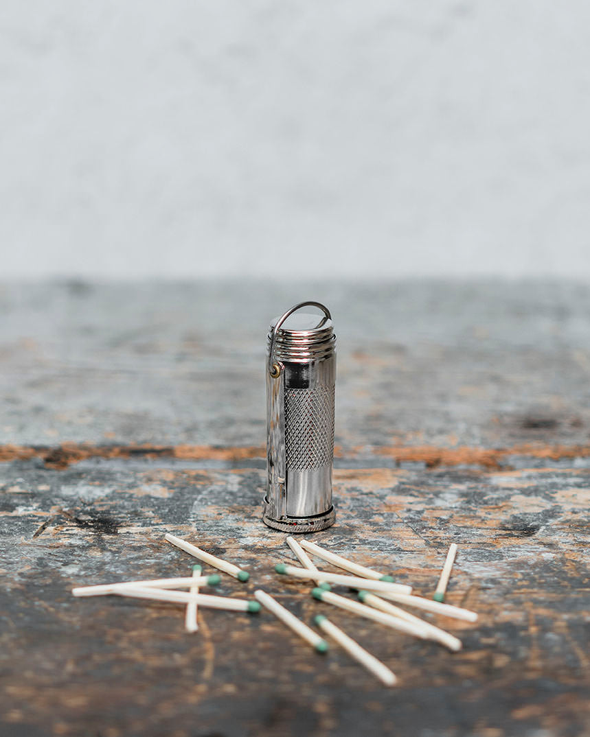 Metal waterproof matchstick case on counter with spilled matches