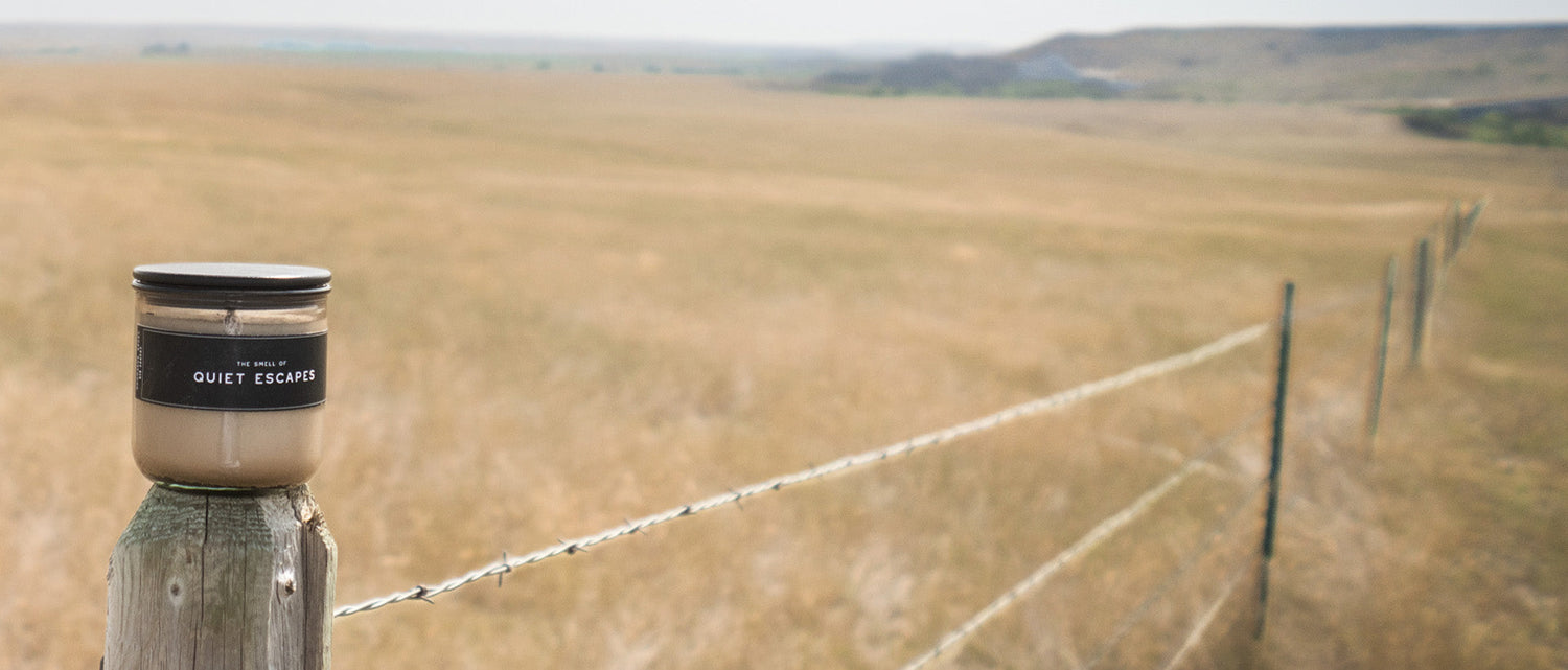 Shoppe 815_The Smell Of Candle Collection - A Quiet Escapes Candle on a fence post with open fields in the background