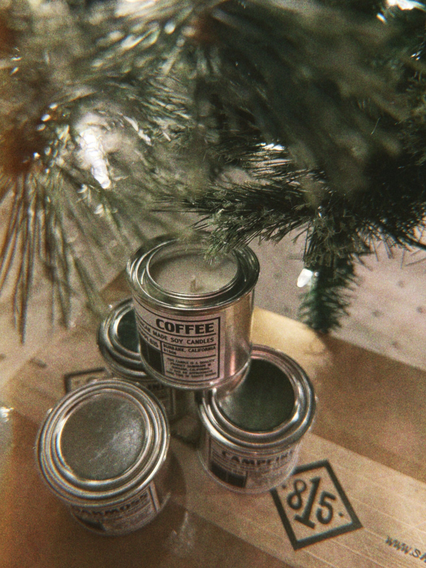 A stack of Shoppe 815 Tin Votive Candles, Coffee, oakmoss, campfire, and gasoline,  under the Christmas Tree.