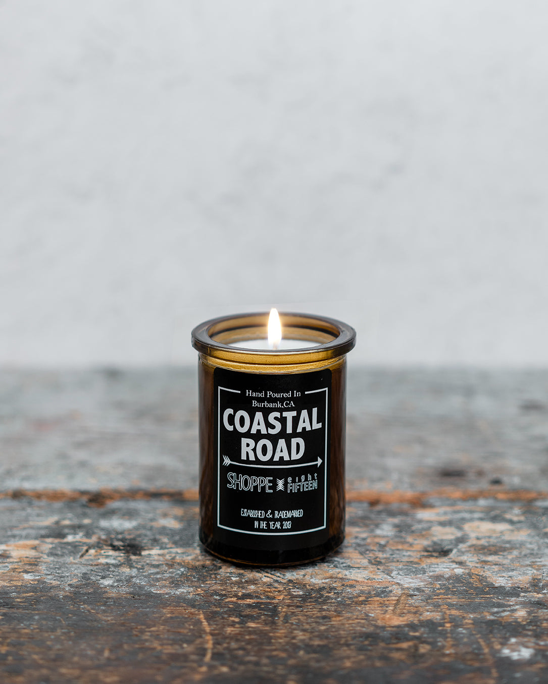 Lit Coastal Road amber glass candle on wooden shelf